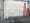 A dead tree emerges out of a grate, against a gray wall and red stepladders.